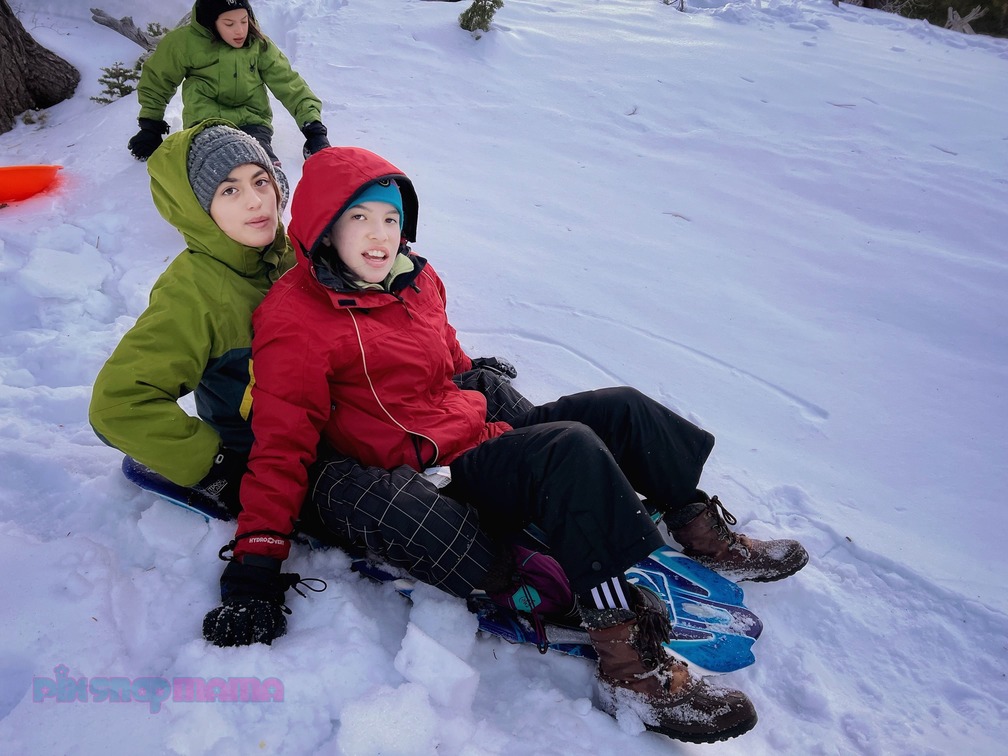 Three girls in the mountains; two on a sled in the woods photographed while taking family snow pictures