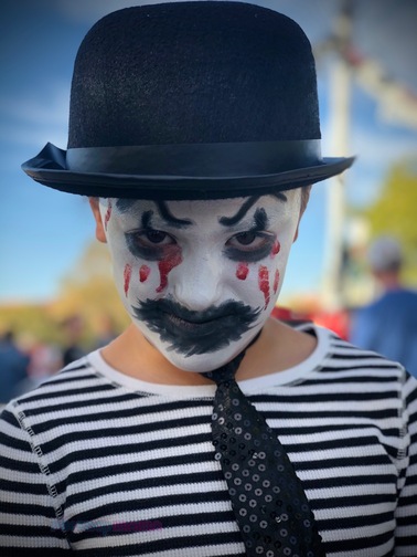 Girl in dressed up as an evil mime in black & white stripped shirt and tie with black bowler hat, white face paint with black accents around her mouth and eyes and red blood dripping down her face