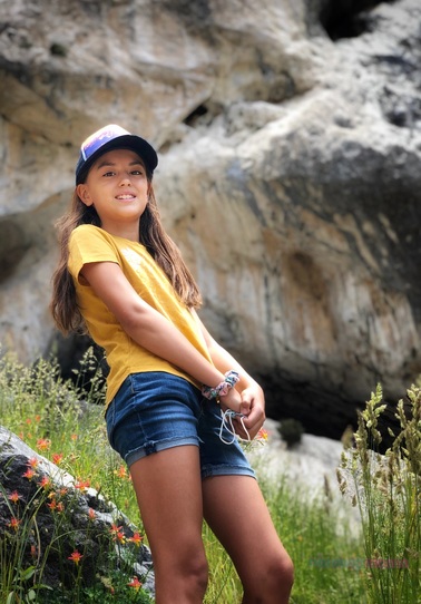 iPhone portraits of a light haired girl in a baseball hat, yellow short sleeve top and jean shorts standing in grass with rocks behind. Pix Snap Mama is overlaid in the lower right corner
