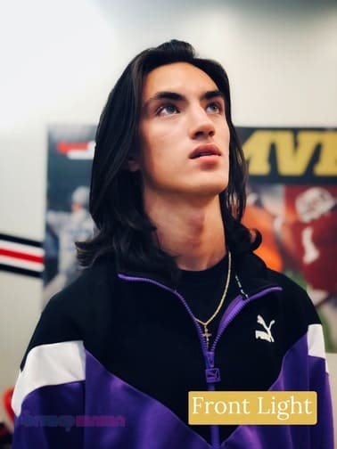 Young man with long dark hair hair wearing a purple, black and white jacket looking up. A front light example of the different types of photography lighting.